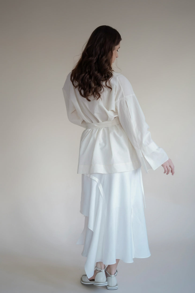 Woman wearing a white outfit with a beige curtain background