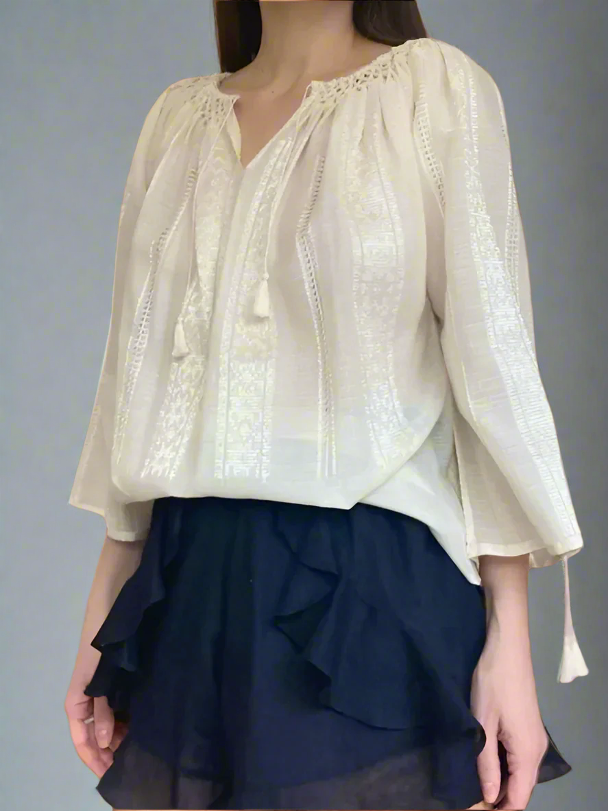 A woman wearing a traditional Romanian blouse in ivory, featuring long sleeves and a honeycomb-pleated collar, paired with a dark skirt.